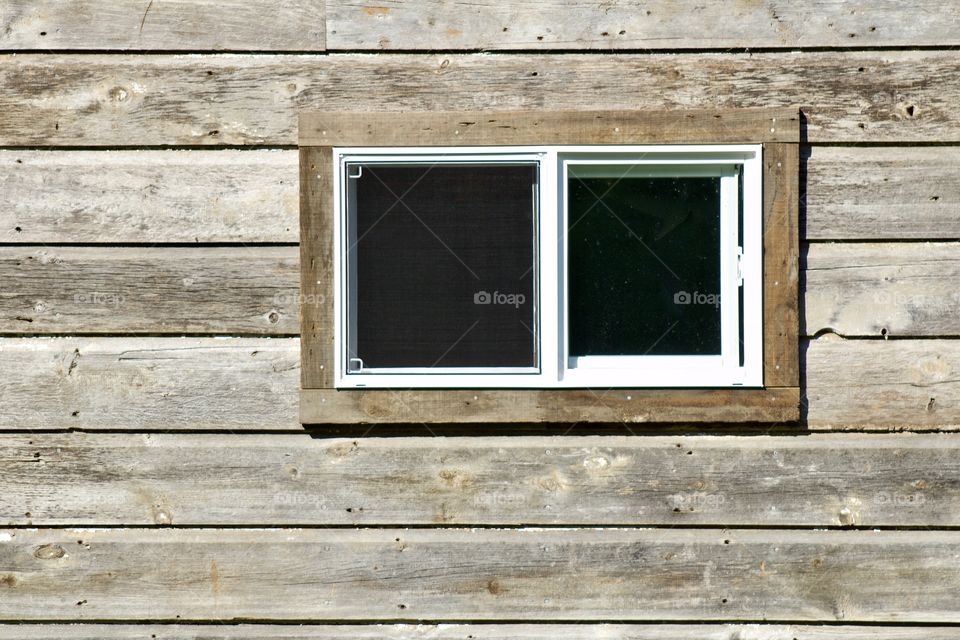 A small double-paned, horizontal window on weathered wooden siding in bright sunlight - landscape