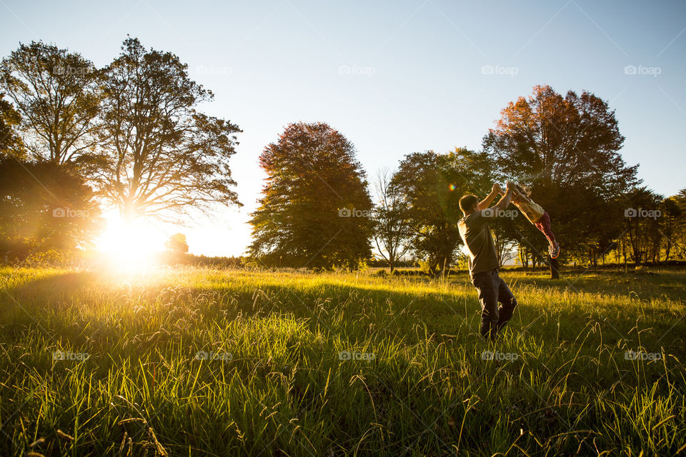 Dad and his girl playing at sunset in a field of long grass with sun through the trees.