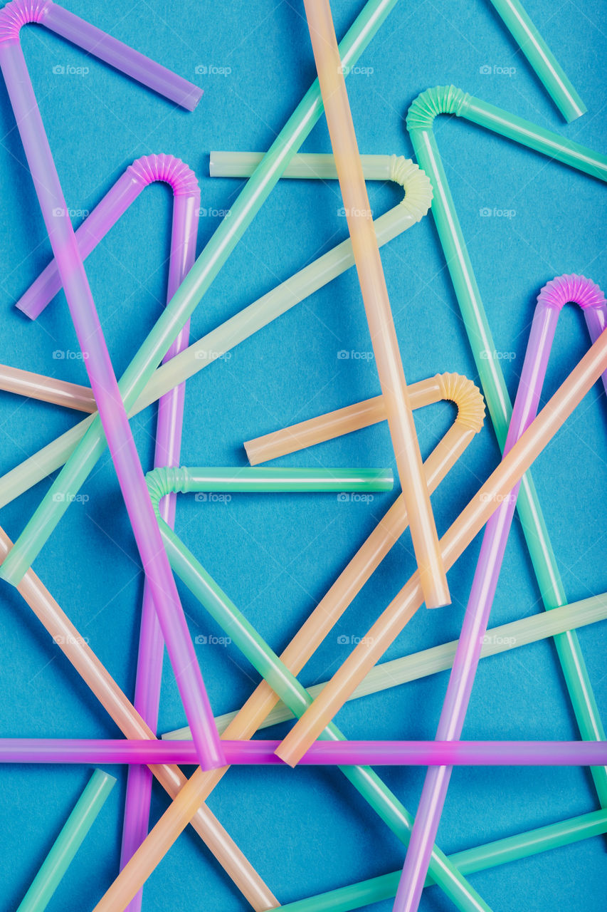 Heap of plastic drink straws scattered over blue background. Collecting plastic waste to recycling. Concept of plastic pollution and too many plastic waste. Copy space at the top