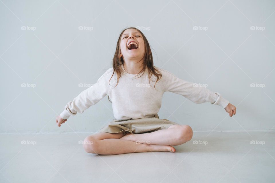Screaming emotional little girl with long hair in natural tones clothes at the light studio