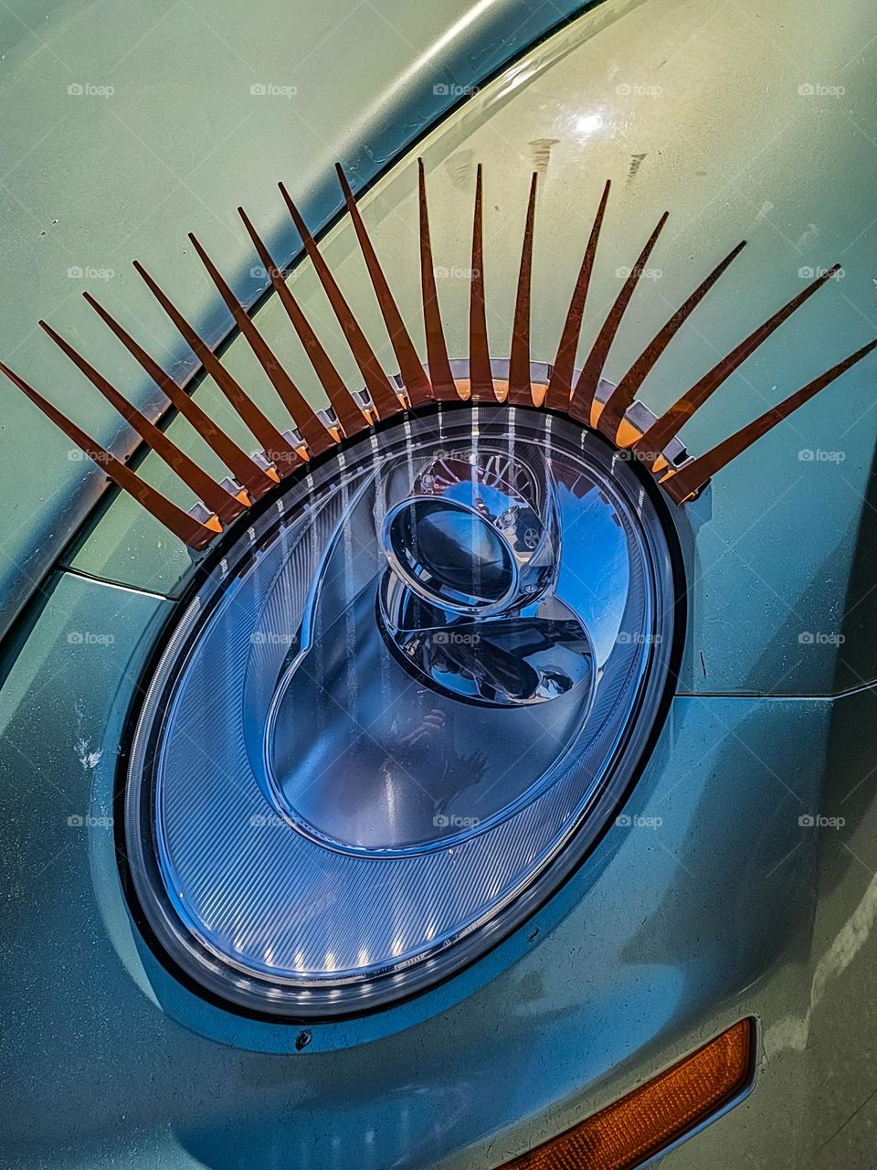 Detail of a pastel green Volkswagen Beetles headlight with eyelashes and a soft reflection in the glass, sorta looks like a cartoon or anime character