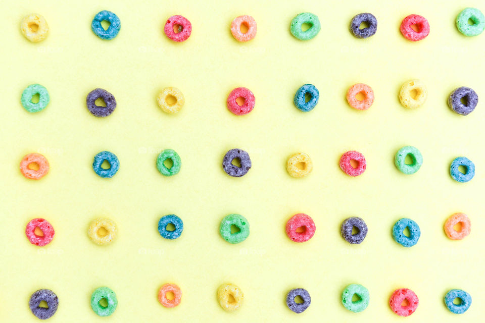 Flat lay of rows of colorful cereal rings on a yellow background