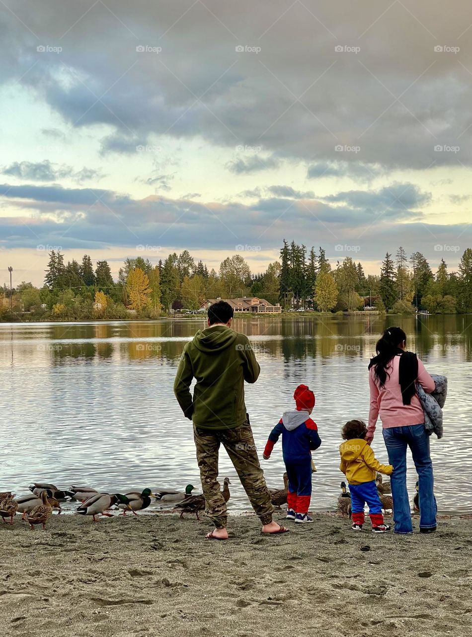 Family with two kids feeding ducks at the lake in autumn 