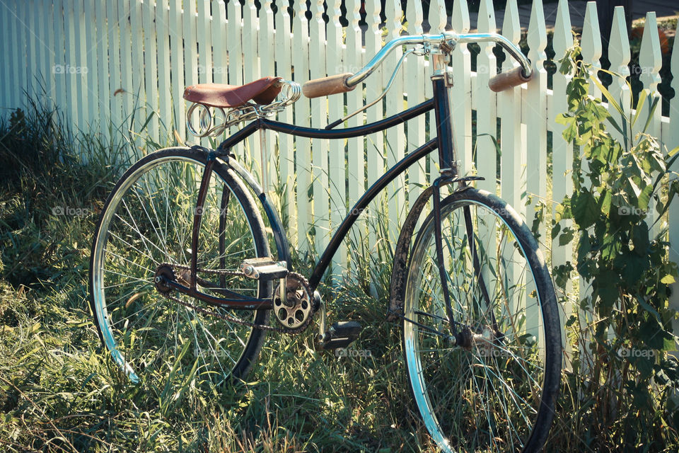 Old-fashioned bicycle leaning on a white picket fence