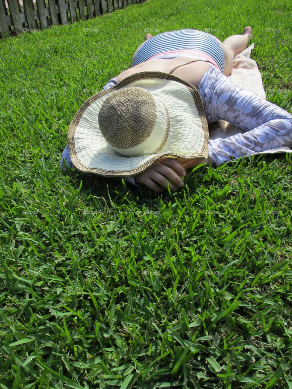 Female in long sleeved swimsuit and sunhat lying in green grass on a sunny day