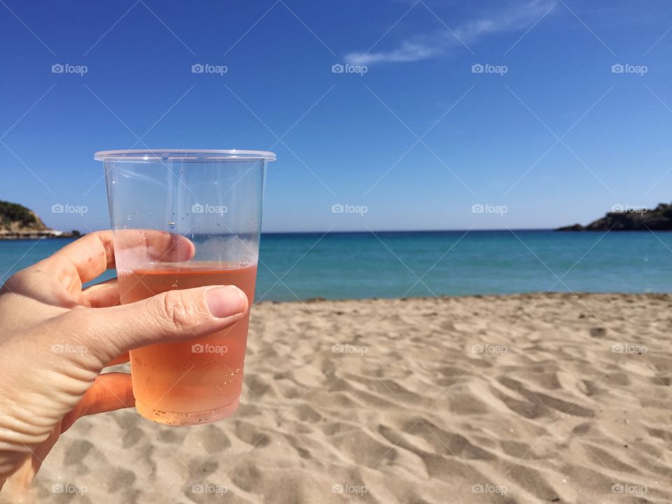 Person holding rose wine at beach
