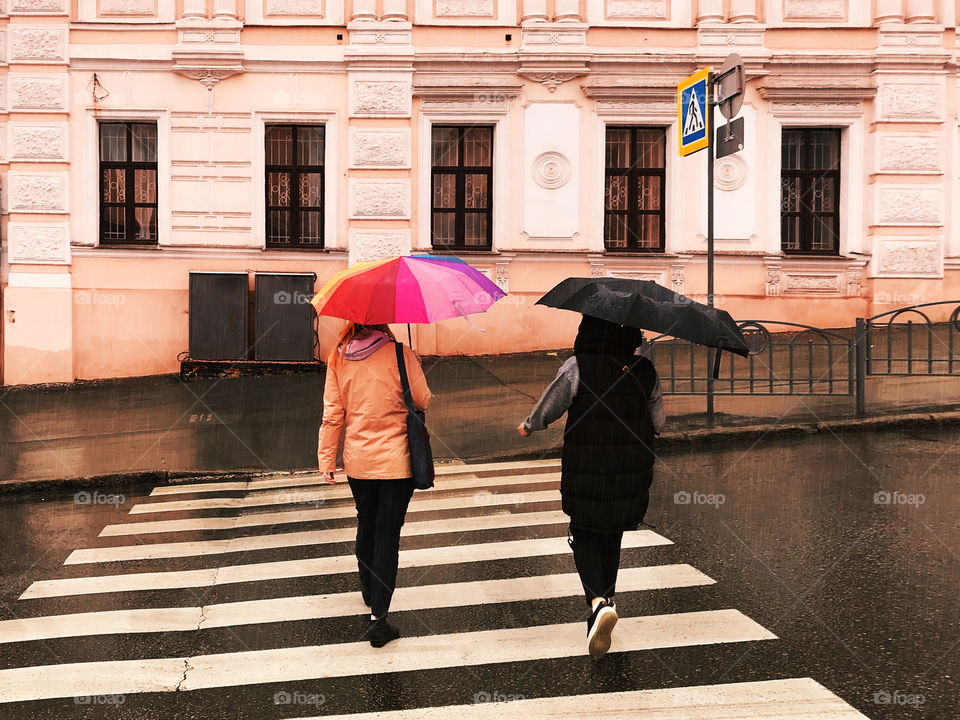 Crossing the road with umbrella in front of a pink old building 