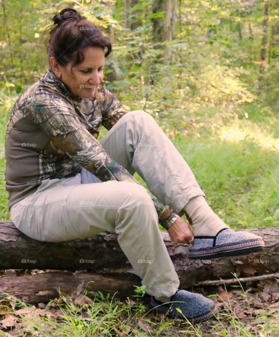 A woman stopping to put her shoes on while hiking 