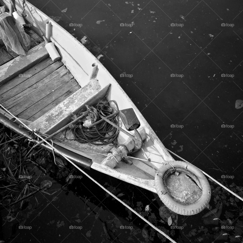 Close-up of front side of small fisherman boat moored in port. Small row boat floating. Black and white photography.