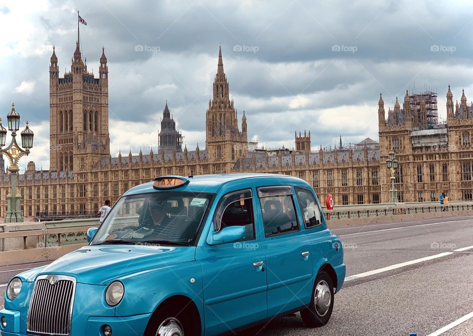 London blue cab proceeding along the street with the Houses of Parliament in the background 