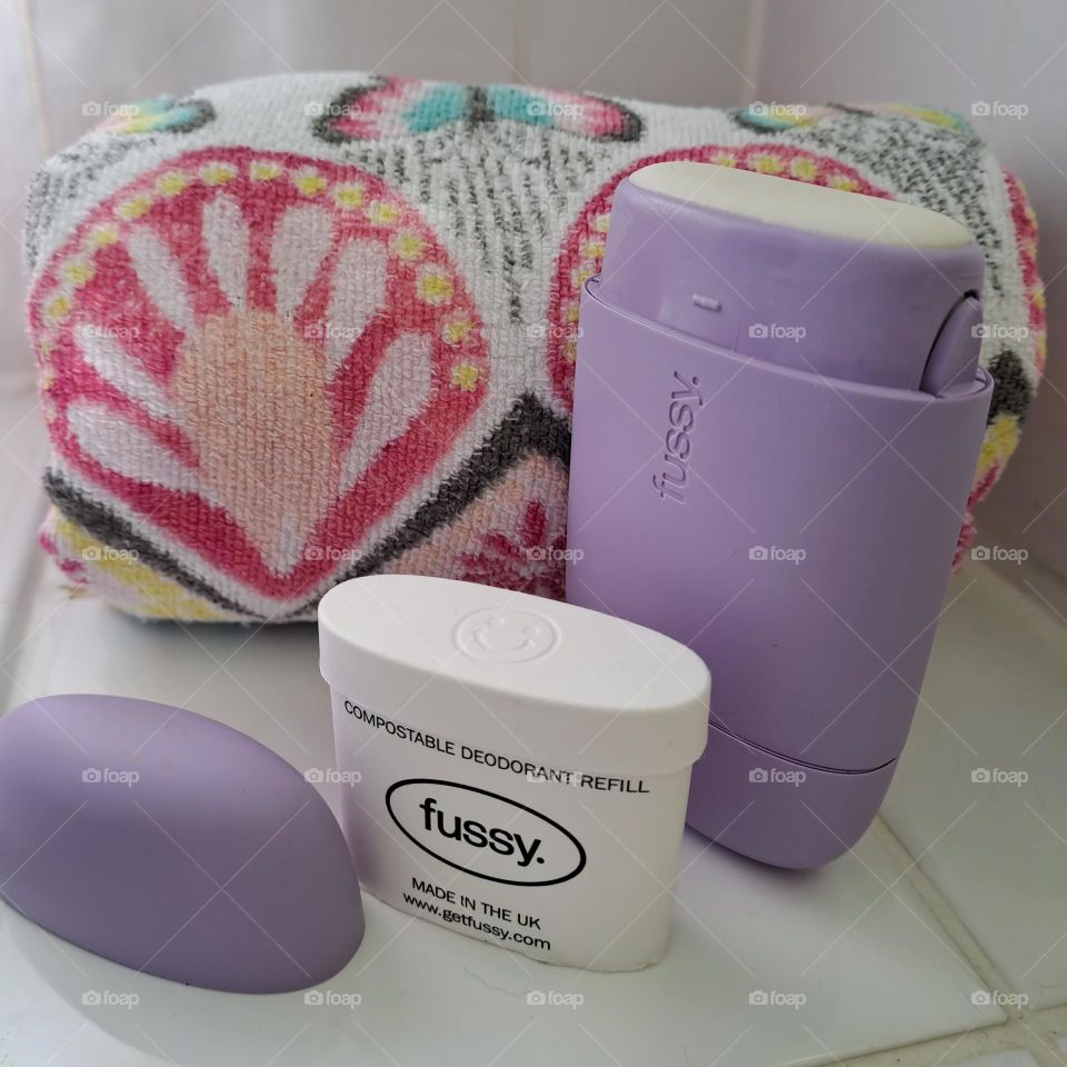 Fussy brand deodrant roll on stick on barhroom tiles with a towel displayed.