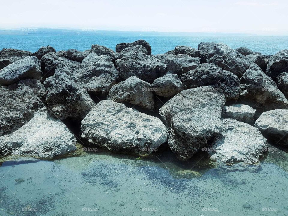 A large wall of rocks breaks the water and are revealed fully by the out going tide. a pool of water sits behind it.