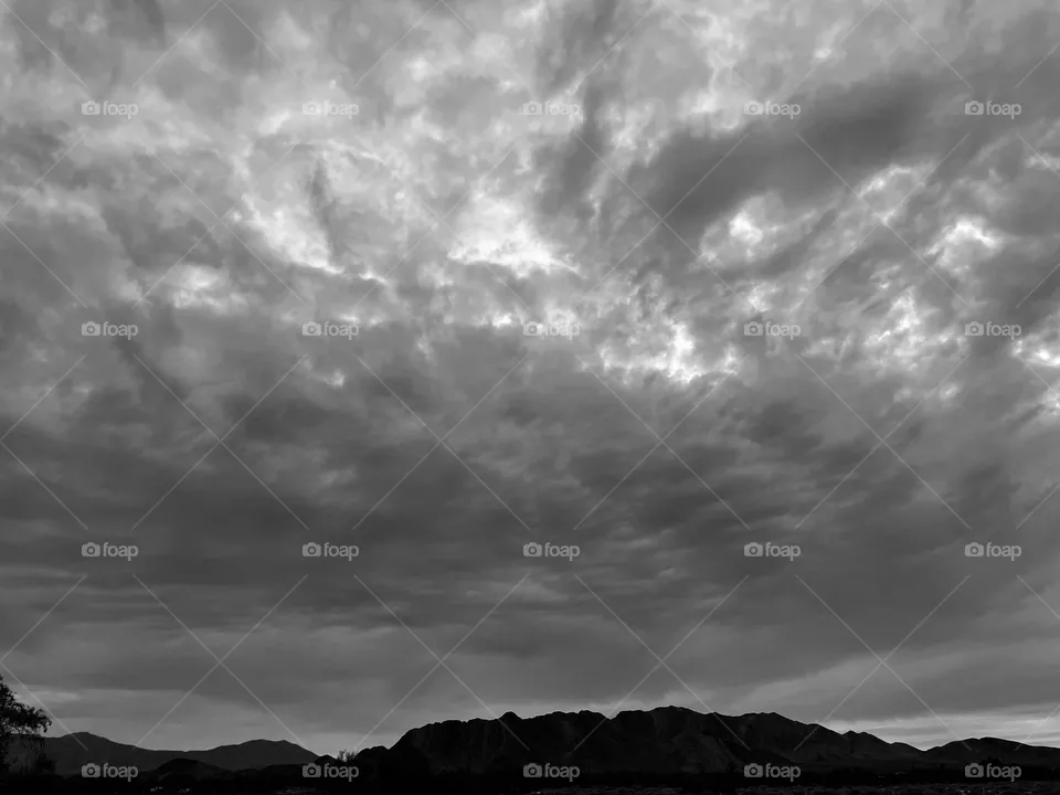 A black and white photo of a mountain with a cloudy sky above. 