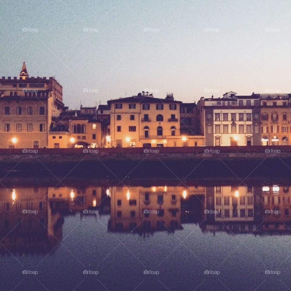 Reflections of homes and stores in the Arno river in Florence at sunset