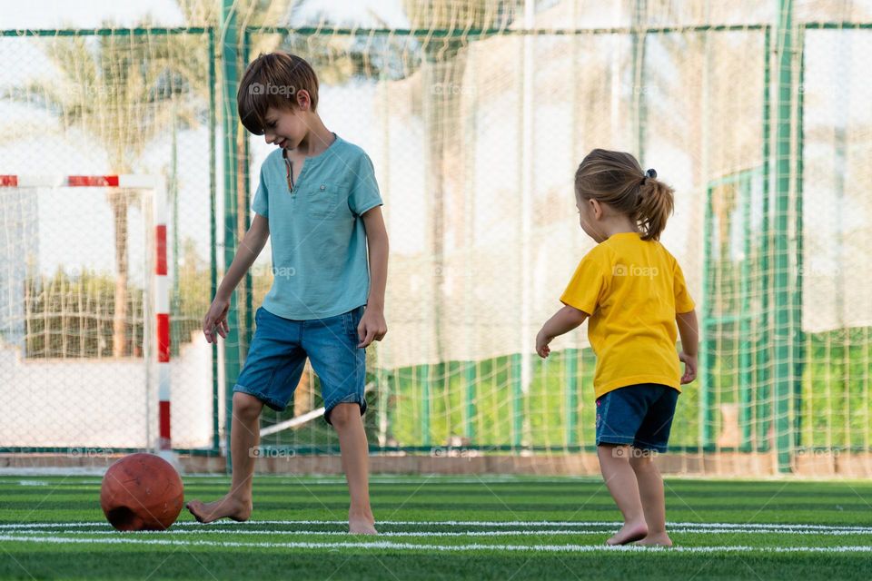 Brother and sister playing football on green lawn.