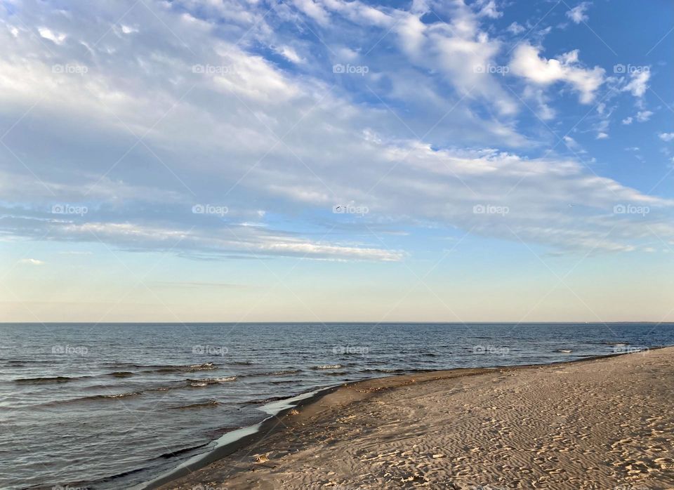 Liquid Fresh water Lake Eerie on Cedar Point shoreline and sandy, rocky beach with blue sky divided by a white cloud