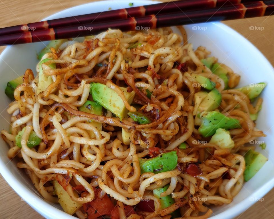 Fried noodles with avocado in a bowl.