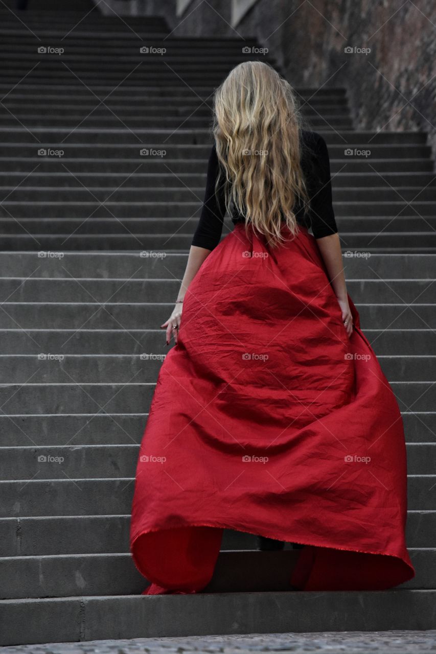 Blonde long hair woman in long red skirt standing on the stairs in old Prague