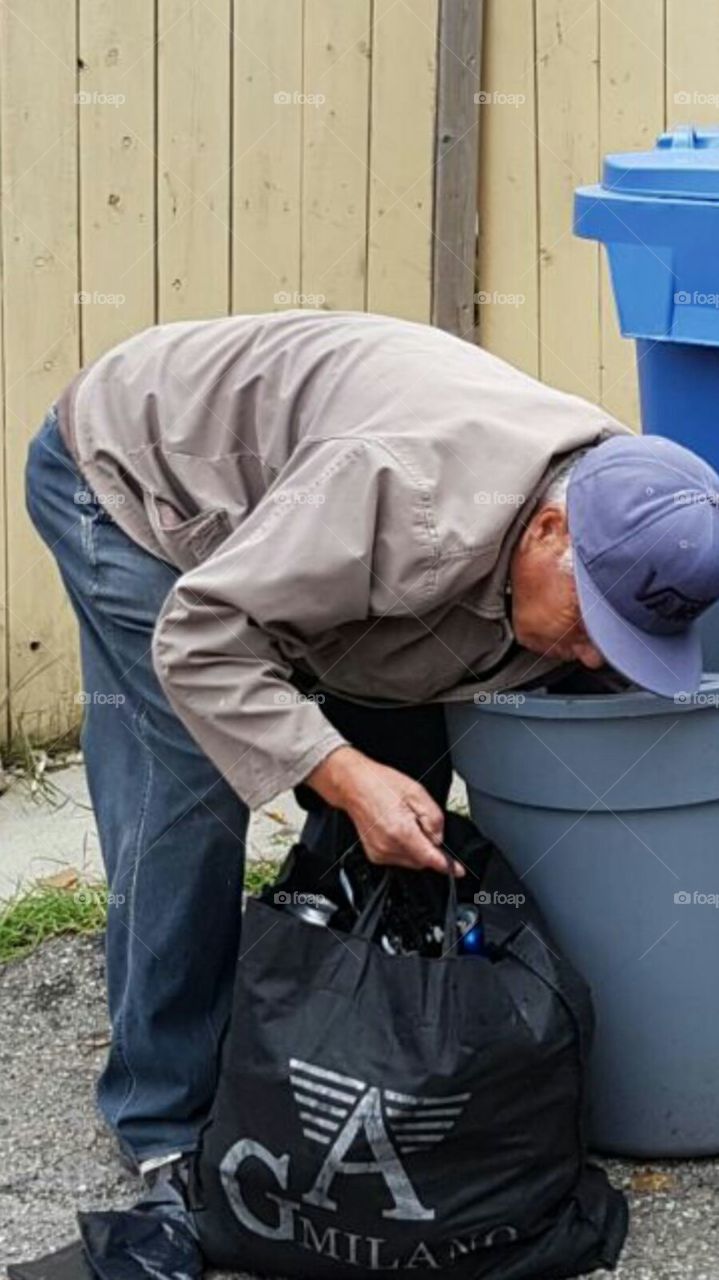 Retiree looking for recyclable bottles and cans in trash bin garbage bin