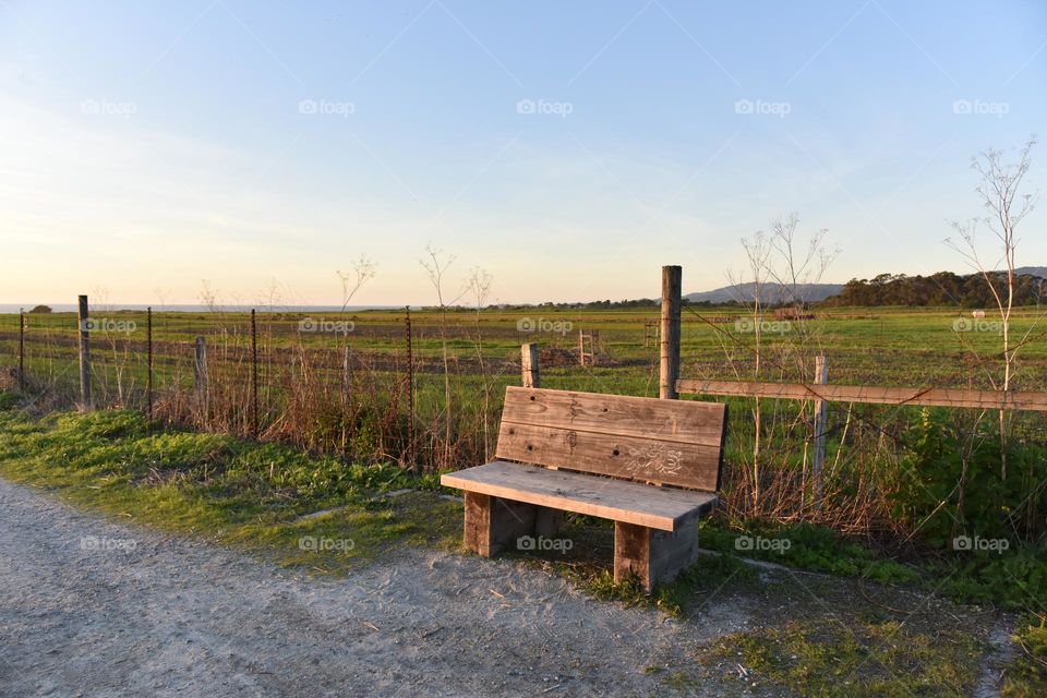 A rustic bench along side a fallow farmland for farmers to rest upon.