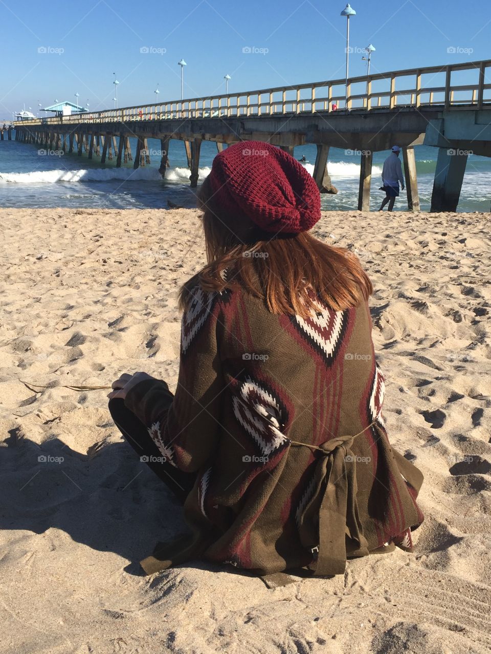 Cool day at the beach..,girl sitting on the beach looking out at the water while being bundled up. 