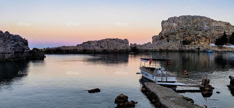 Beautiful panoramic view of the sunset mediterranean sea with rocks and a boat in the bay of St. Paul in the city of Lindos on the island of Rhodes Greece, close-up side view.