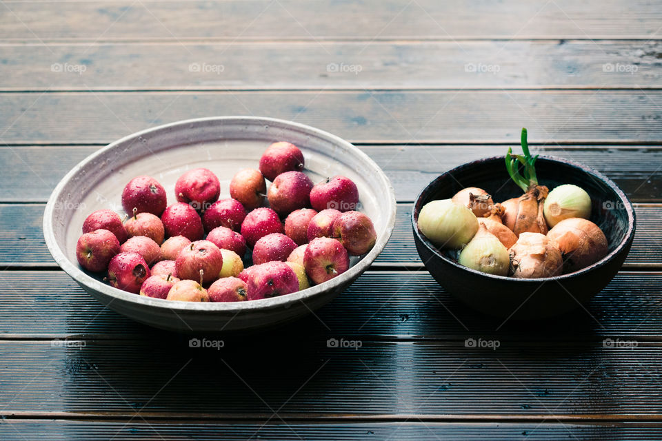 Closeup of bowls of fresh red apples and onions sprinkled raindrops on wooden table