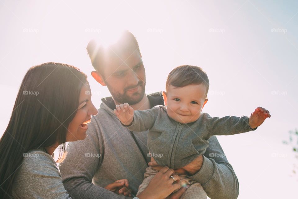 Happy family with cute baby boy on sky background outdoors, sensitivity to the nature concept
