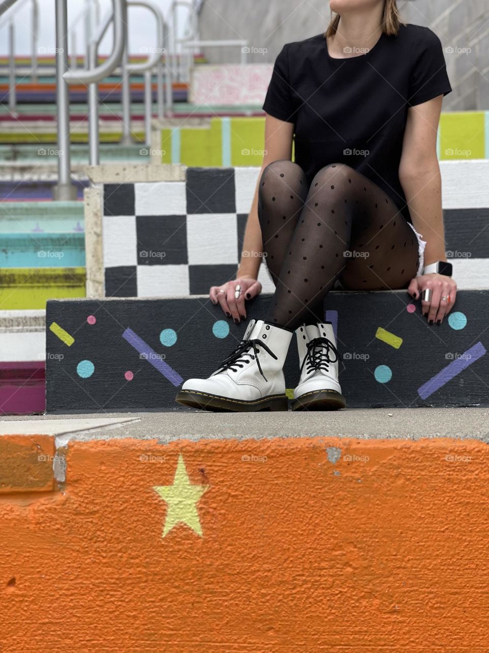 Woman sitting on colorfully painted stairs outdoors in an urban setting wearing Dr. Martens