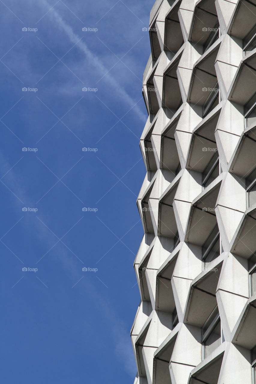 Vapour trails left by planes, against the jagged facade of a building in central London, UK