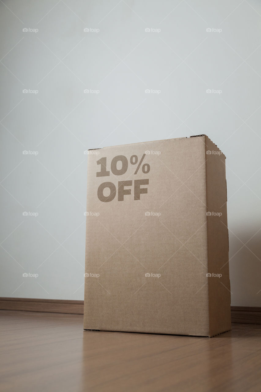 Cardboard box with 10% off order written on the box placed on the floor in an empty room with a neutral background. delivery concept. economy concept. business concept. shopping concept. copy space.