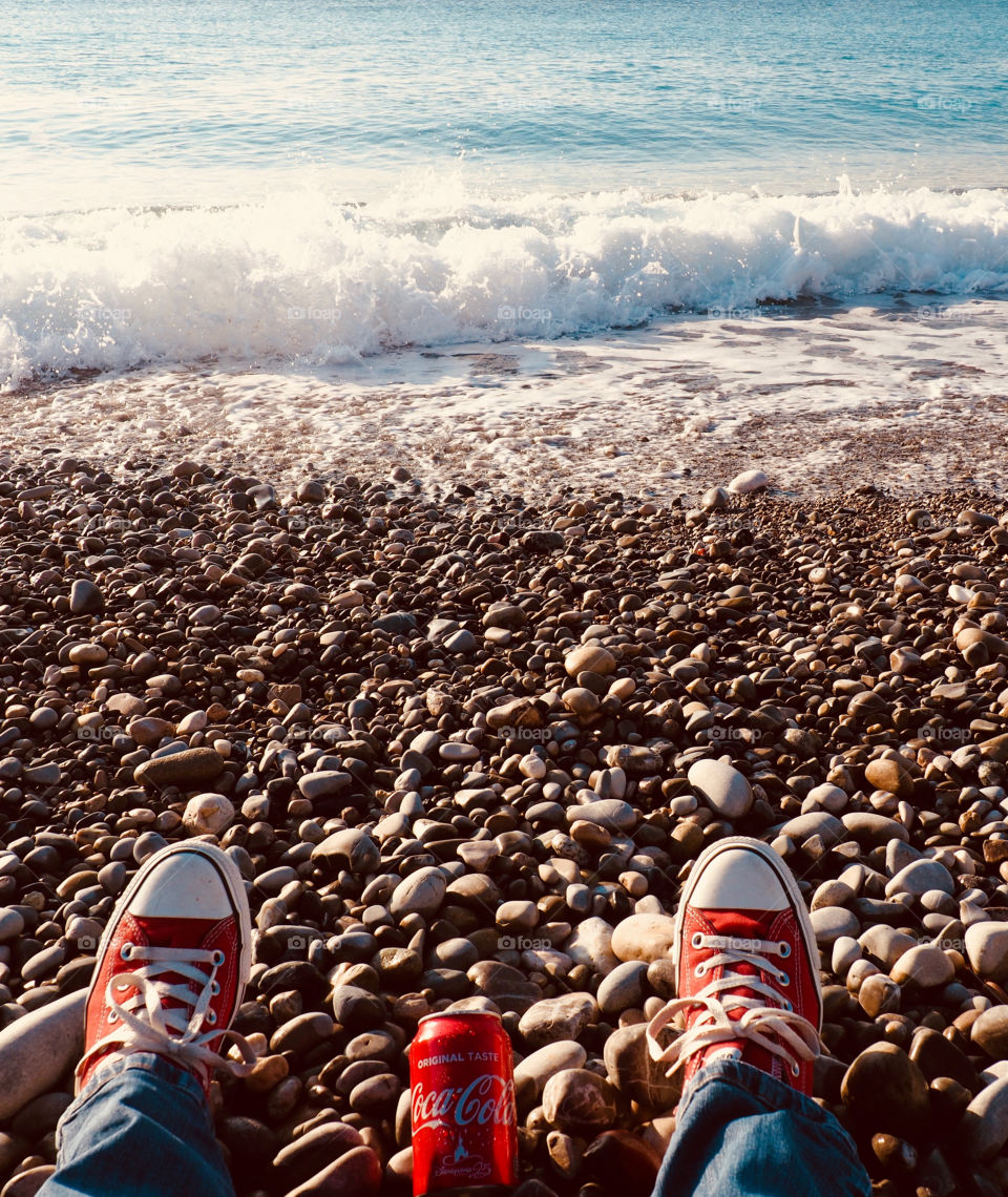 A can of Coca Cola on the beach in Nice with red sneakers.