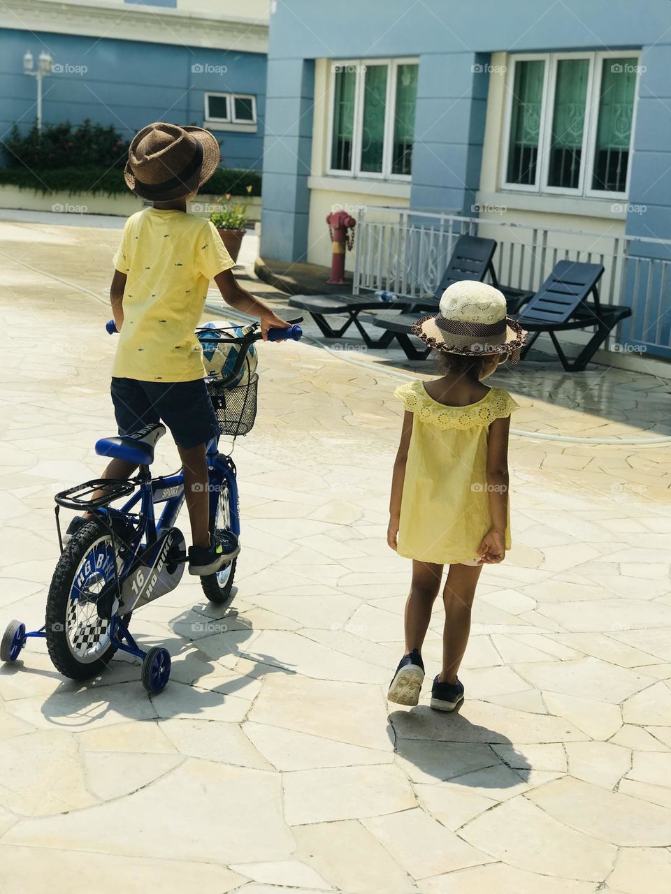 A boy and girl both are in a yellow summer outfits and walking towards straight and both are having chats on their heads.