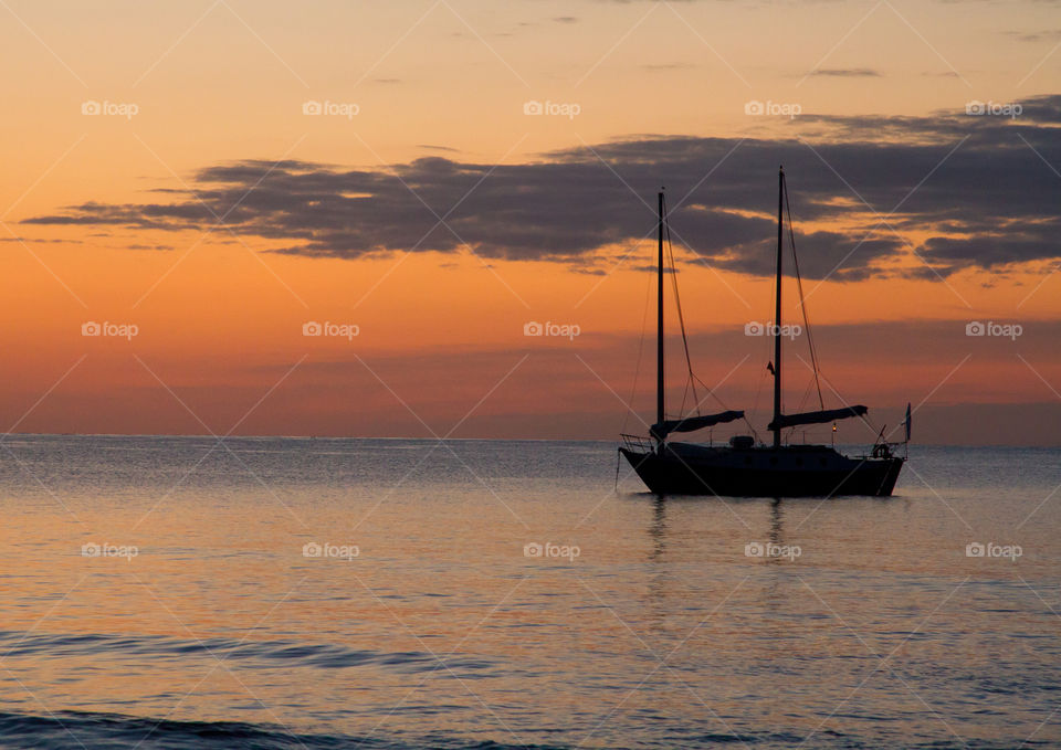 Sailing Boat Sunrise. A sailing ship floats on a calm Ocean as the sun rises.