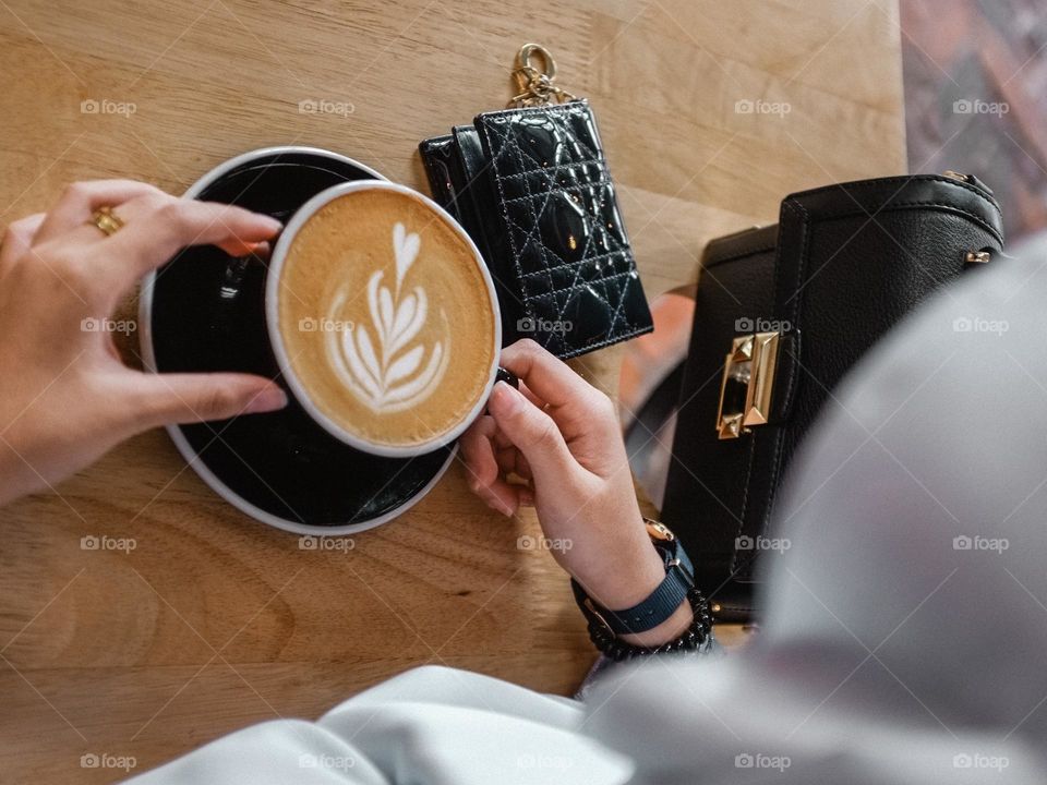 A high angle view of a woman holding a cup of coffee latte in a restaurant