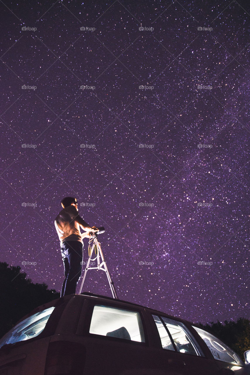 A photographer Stargazing at the milkyway during a summer night ontop of his car