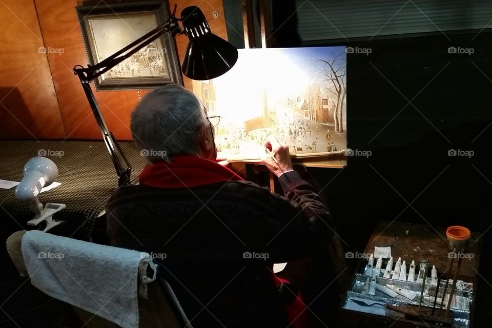 A painter in Antibes, France is working on his paint under a lamb light at night.