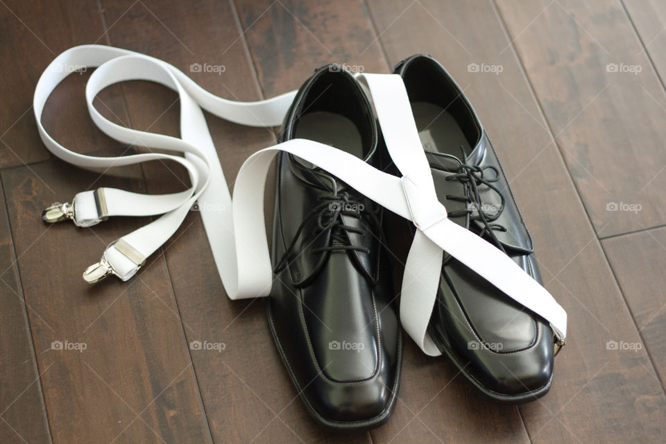 A grooms shoes and suspenders on a hardwood floor