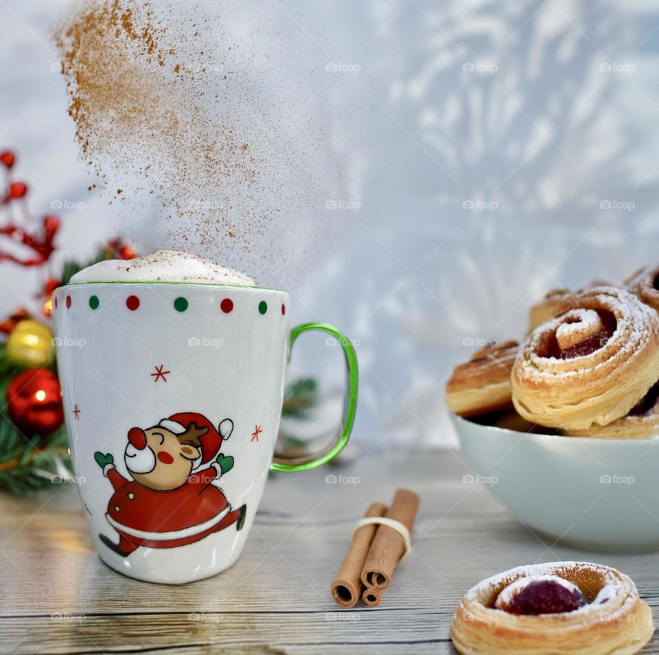 New Year's cup with cappuccino and cinnamon stands on the table next to a plate with pastries on a New Year's background.
