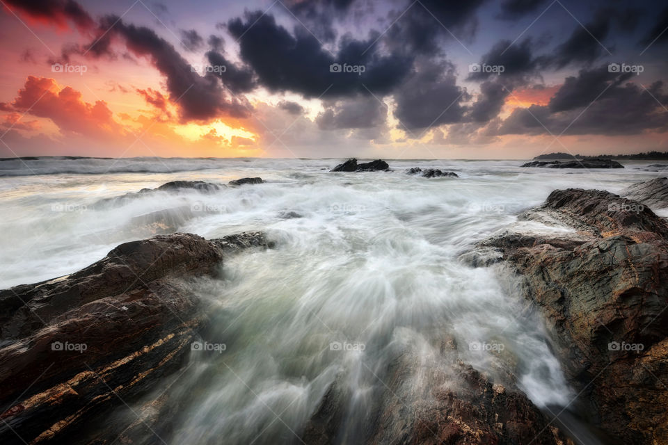Rushing waves with dramatic skies during sunrise over the beach