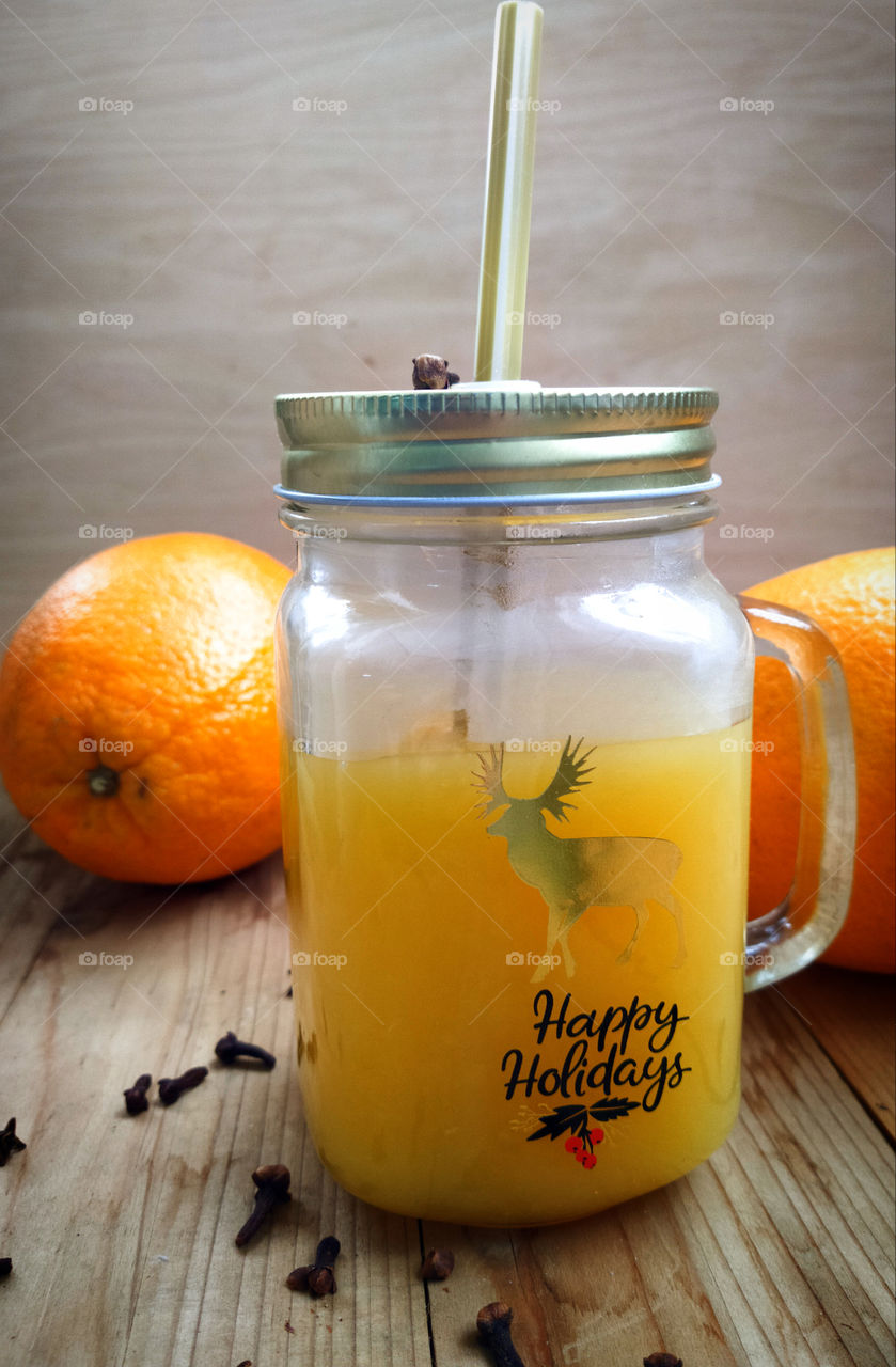 Glass mug with lid with orange juice.  Against the background of two oranges