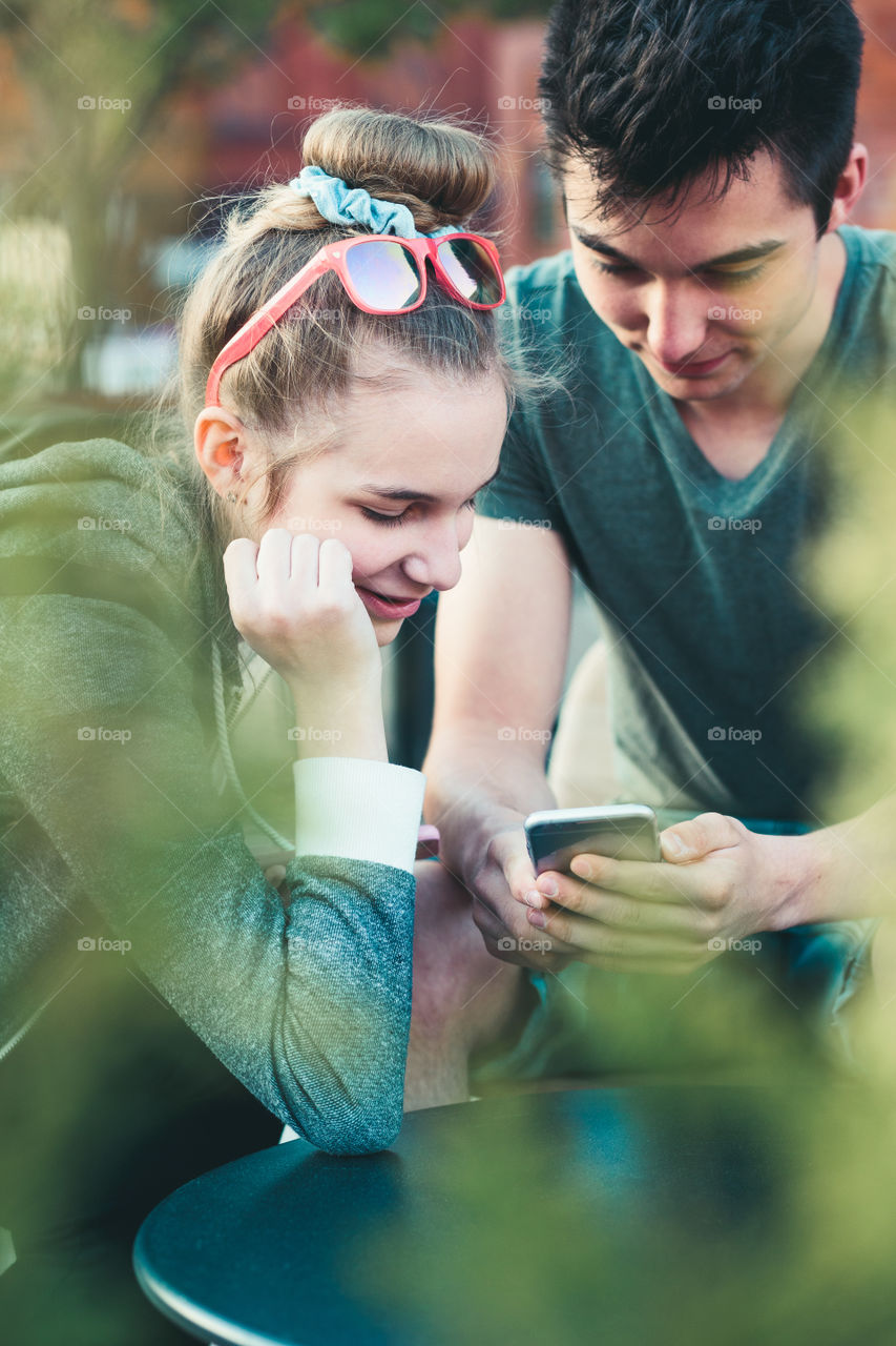 Couple of friends, teenage girl and boy, having fun with smartphones, sitting in center of town, spending time together