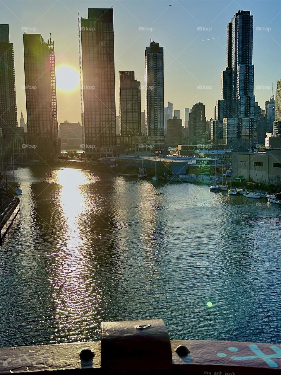 This is „Newtown Creek“ seen from the „Pulaski Bridge“ that connects „Greenpoint“, Bklyn to LIC. In the golden hour of sunset the „E River“ shimmers in metallic tones of silver and gold. In the distance we see „Manhattan“. 2024. Hypnotic Productions