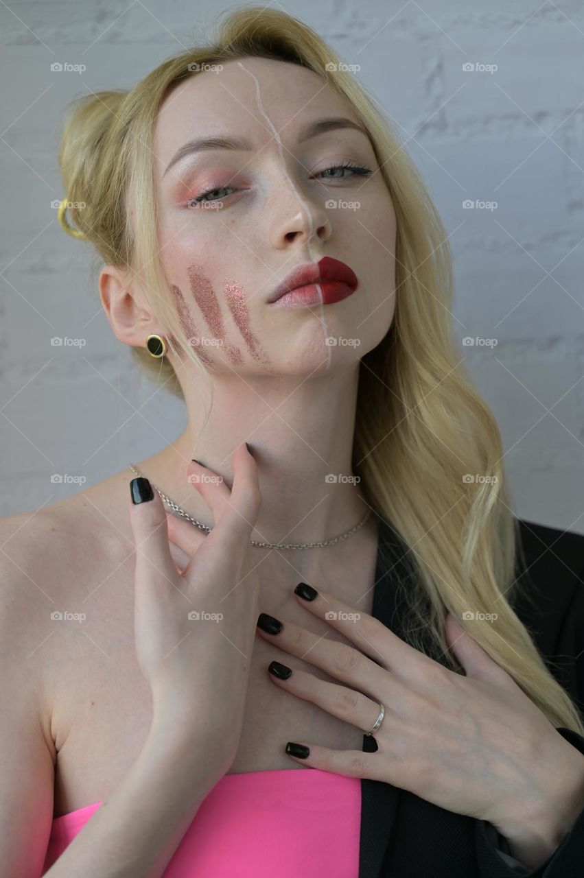 Close-up portrait of a blonde girl with different make-up on half of her face with hand on the neck on white background