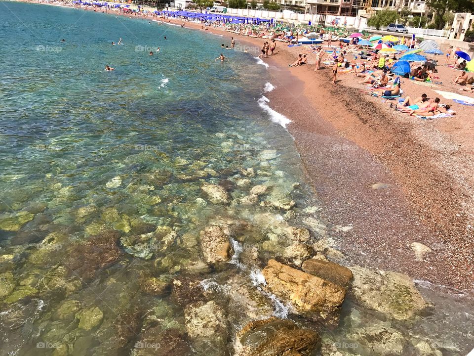Stones and rocks at the beach and a bunch of people just chilling and enjoying by the ocean.