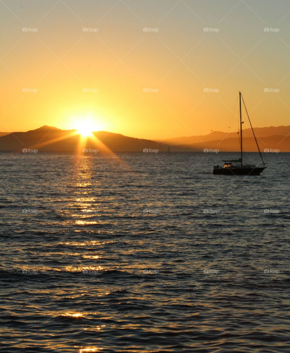 Sunset over mountain and sea with sailboat
