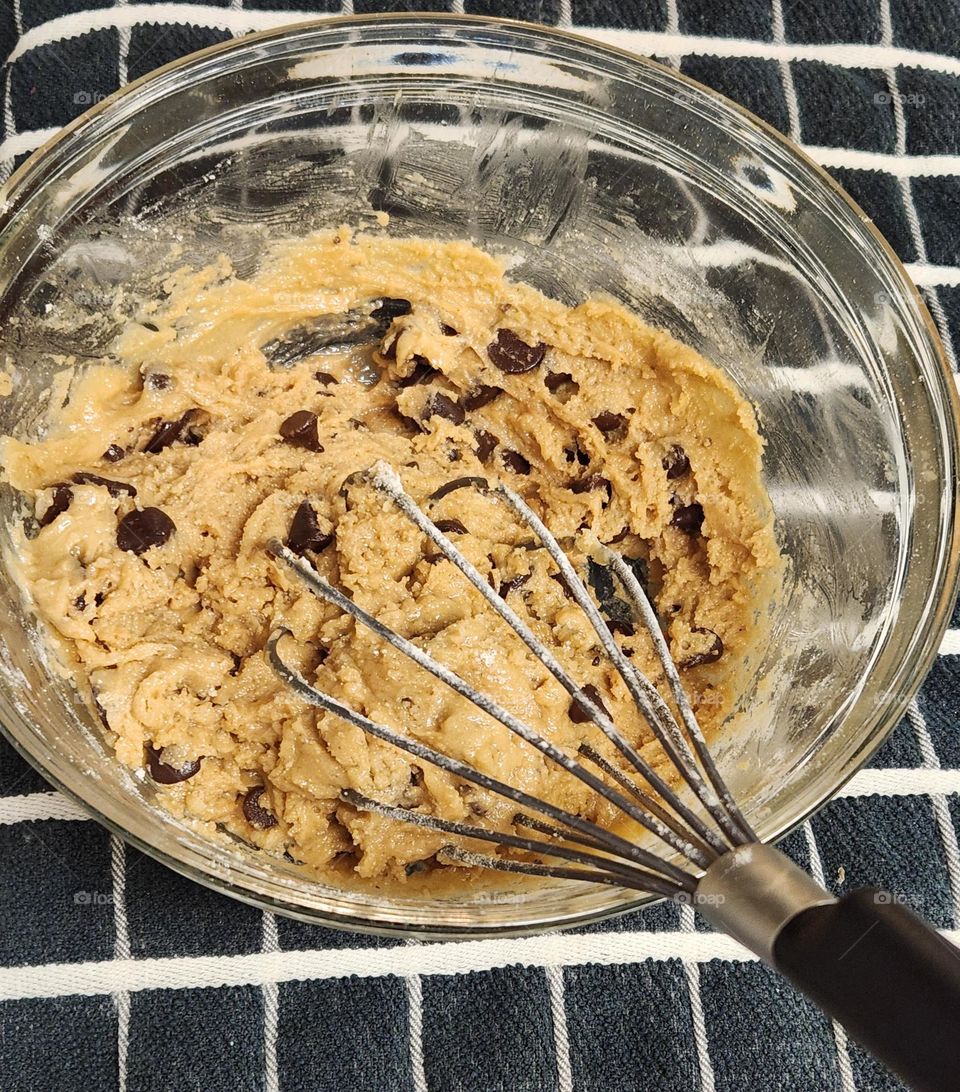 whisk stirring bowl of chocolate chip cookie dough on a kitchen towel for home baking