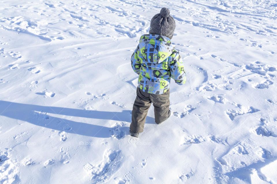 A child in winter in winter jackets, pants, a hat and boots on white snow on the street and in the park in nature plays winter fun and sleds.