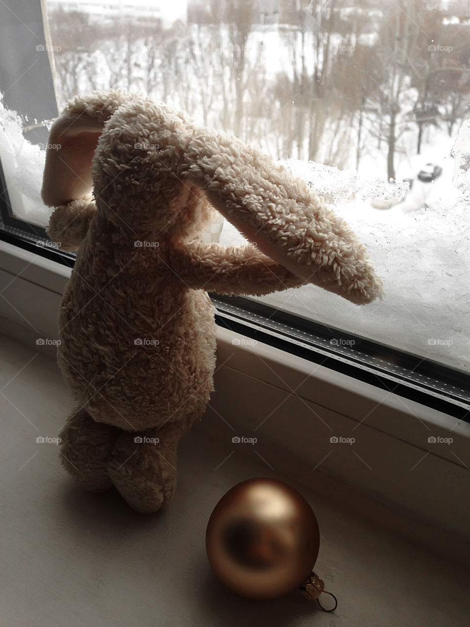 Toy bunny with a Christmas sphere looking at winter weather 