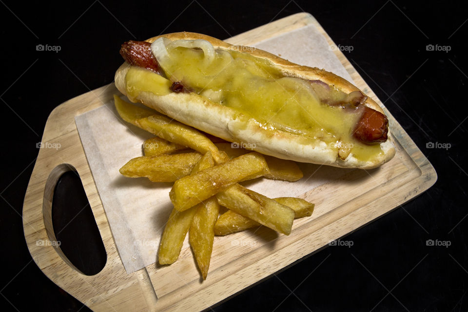 Hot dog and French fries. served on a wooden board isolated on a black backdrop